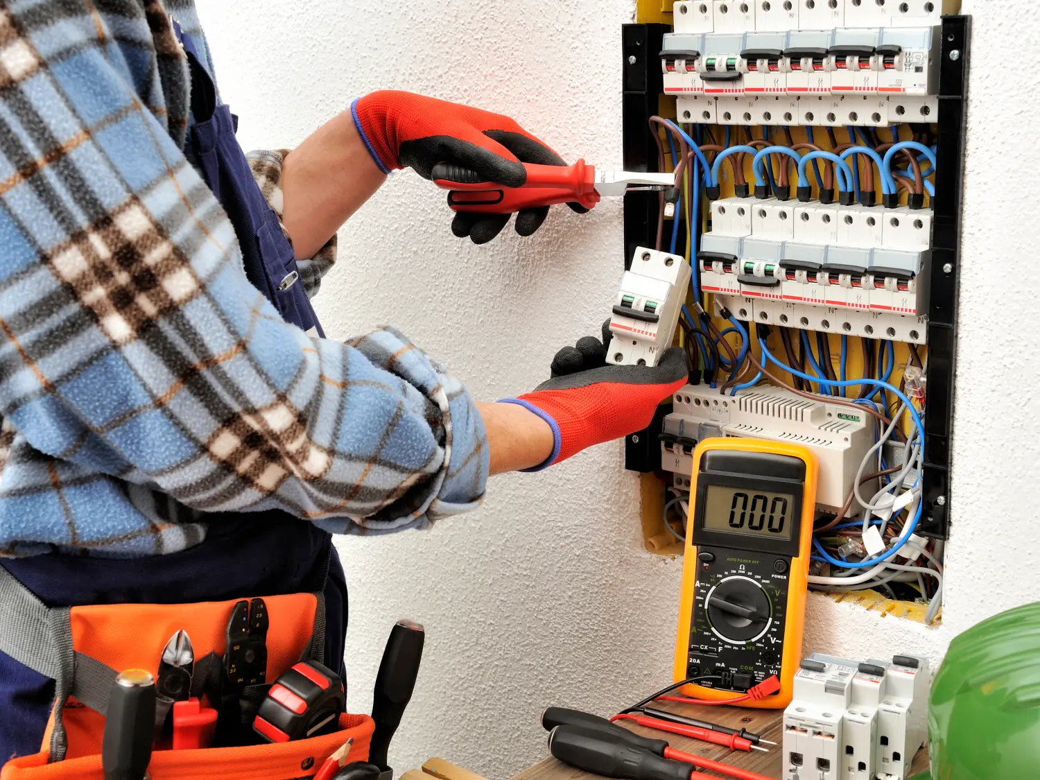 Junger Elektriker bei der Arbeit an einer Schalttafel mit Schutzhandschuhen