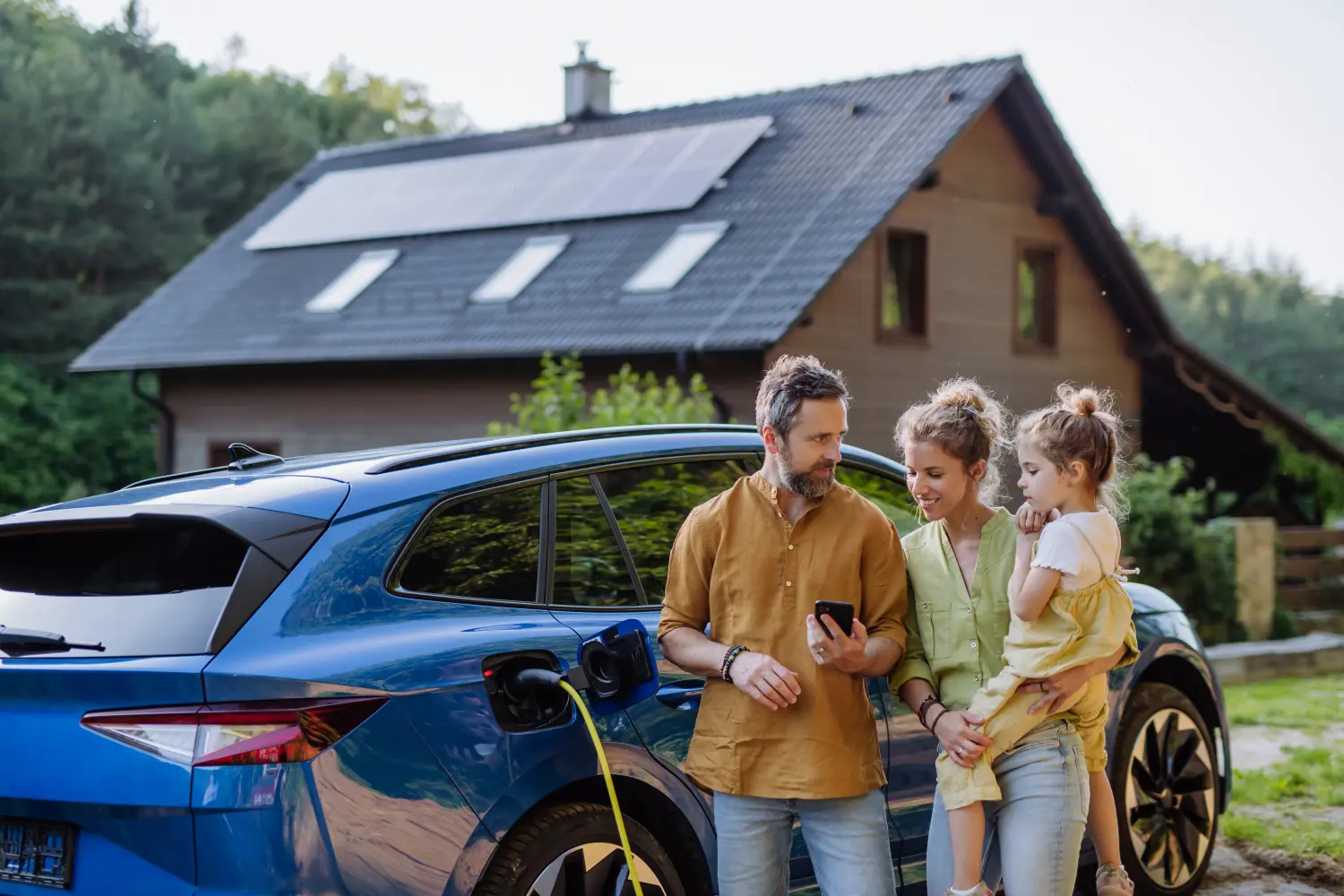 Familie mit kleinem Mädchen steht vor ihrem Haus mit Sonnenkollektoren auf dem Dach und hat ein Elektroauto.